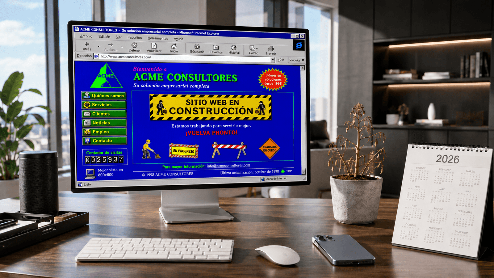 Escritorio moderno con ordenador e iPhone, y en la pantalla una web anticuada de los noventa con cartel de 'en construcción'